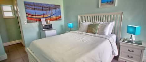 A neatly made bed with white linens, a white headboard, and two bedside tables with lamps.