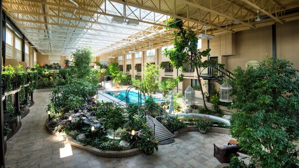 An indoor atrium with a swimming pool, surrounded by lush greenery and a high ceiling with skylights. - Hotel L'Oiseliere Montmagny (Montmagny)
