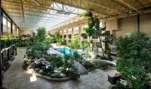 Un atriumo interior con piscina, rodeado de abundante vegetación y un techo alto con tragaluces.