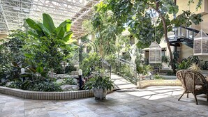 A spacious indoor garden with a variety of plants, a central seating area with a wicker chair, and a glass ceiling structure. - Hotel L'Oiseliere Montmagny (Montmagny)