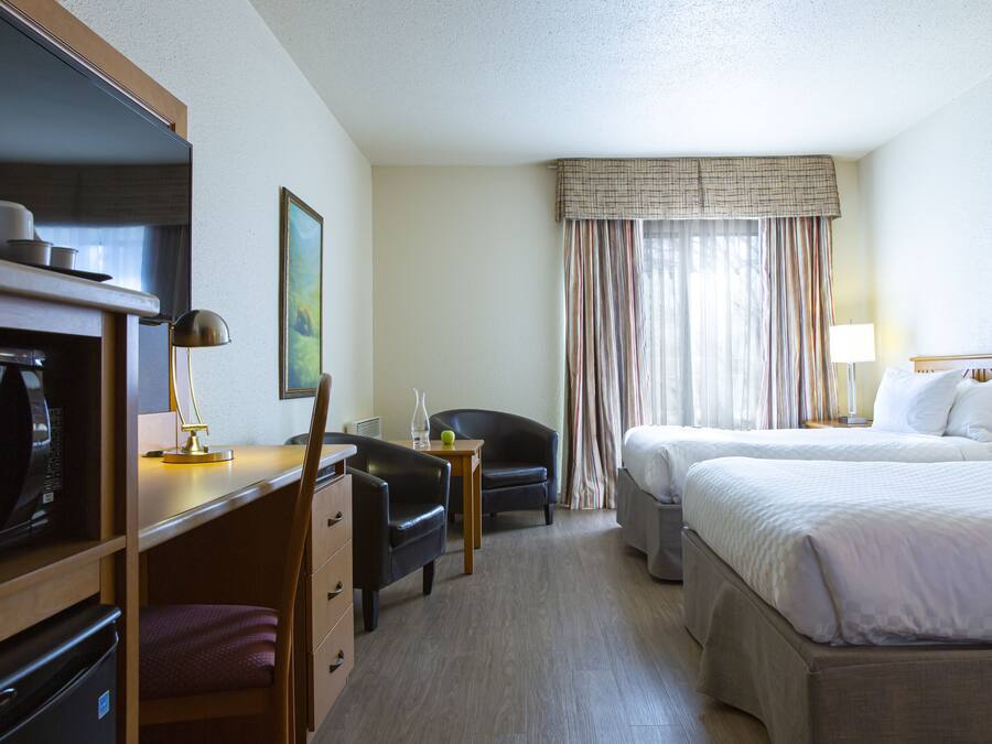 A hotel room with a desk, two chairs, a bed, a TV, and a window with curtains.