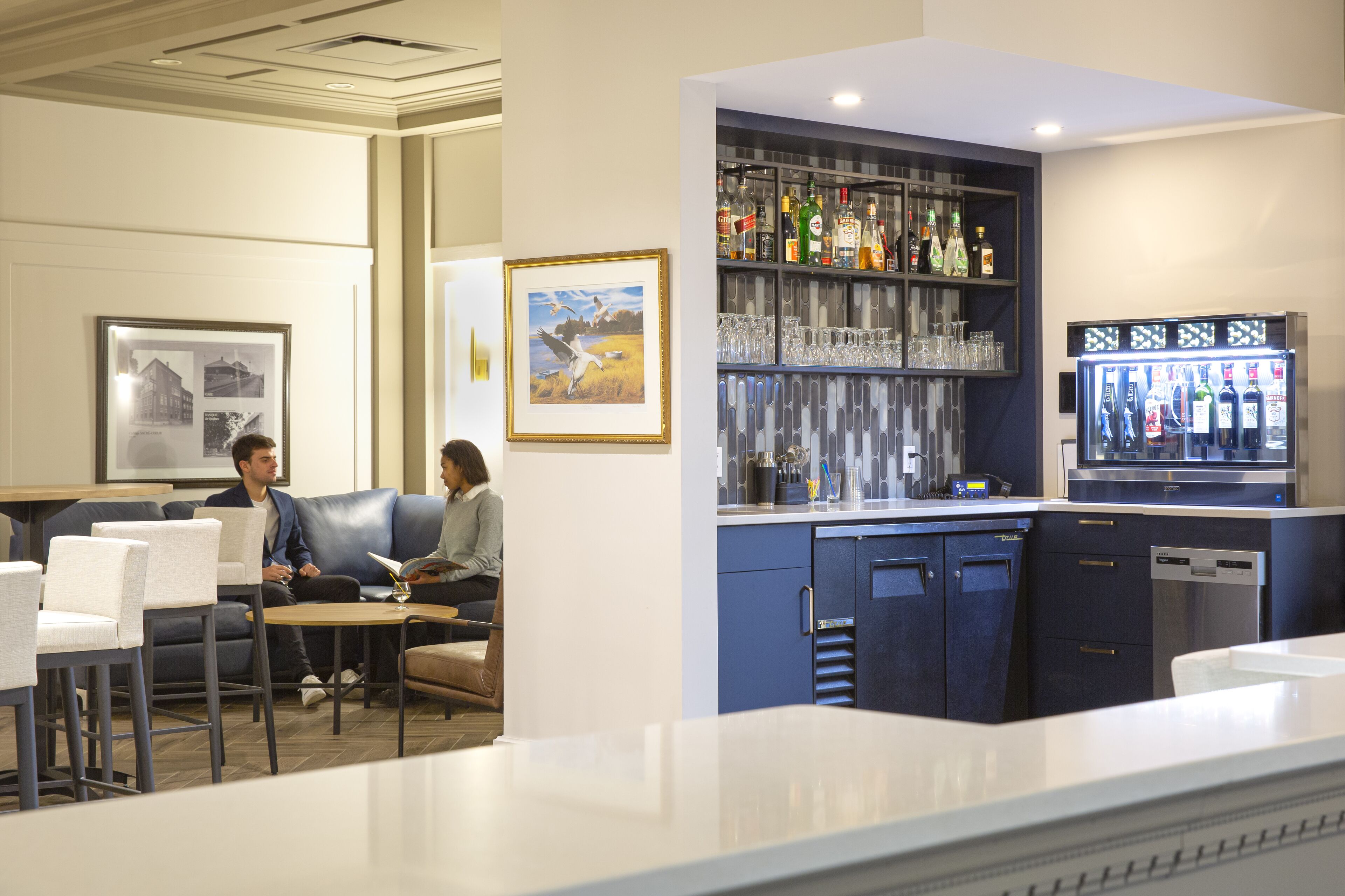Una zona de bar con mostrador, asientos y un refrigerador lleno de bebidas.