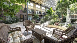 A spacious indoor garden with wicker furniture, a statue, and a variety of plants. - Hotel L'Oiseliere Montmagny (Montmagny)