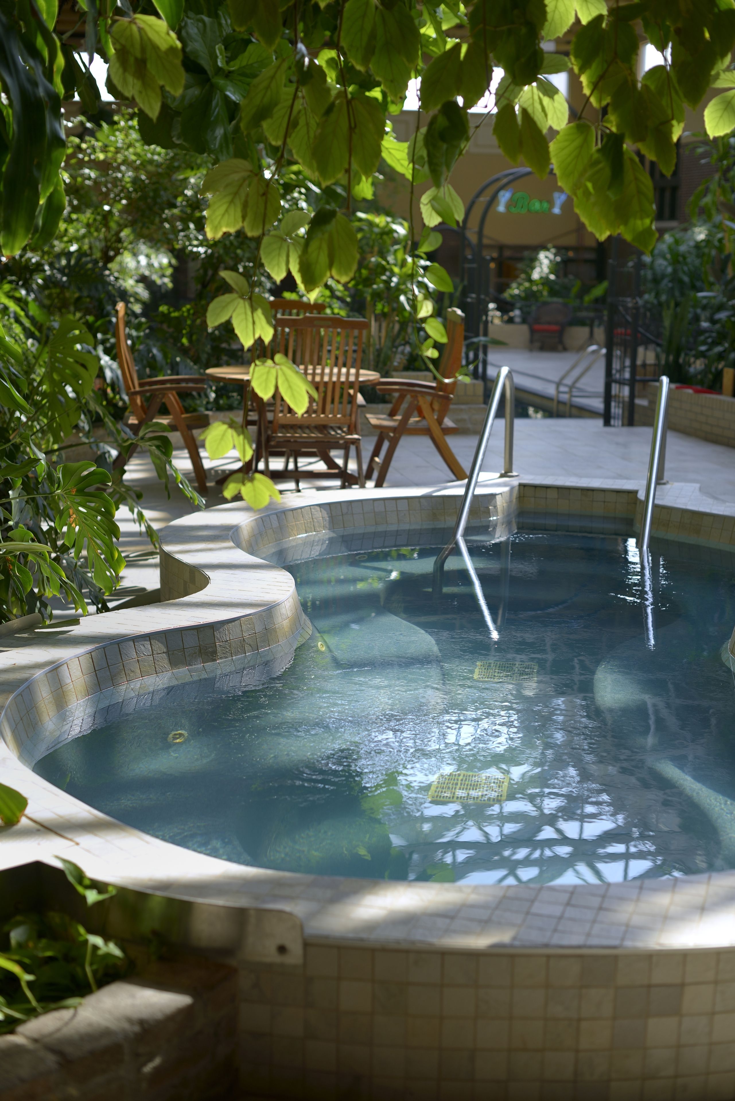 A hot tub area with tiled steps, wooden chairs, and a tiled pool.