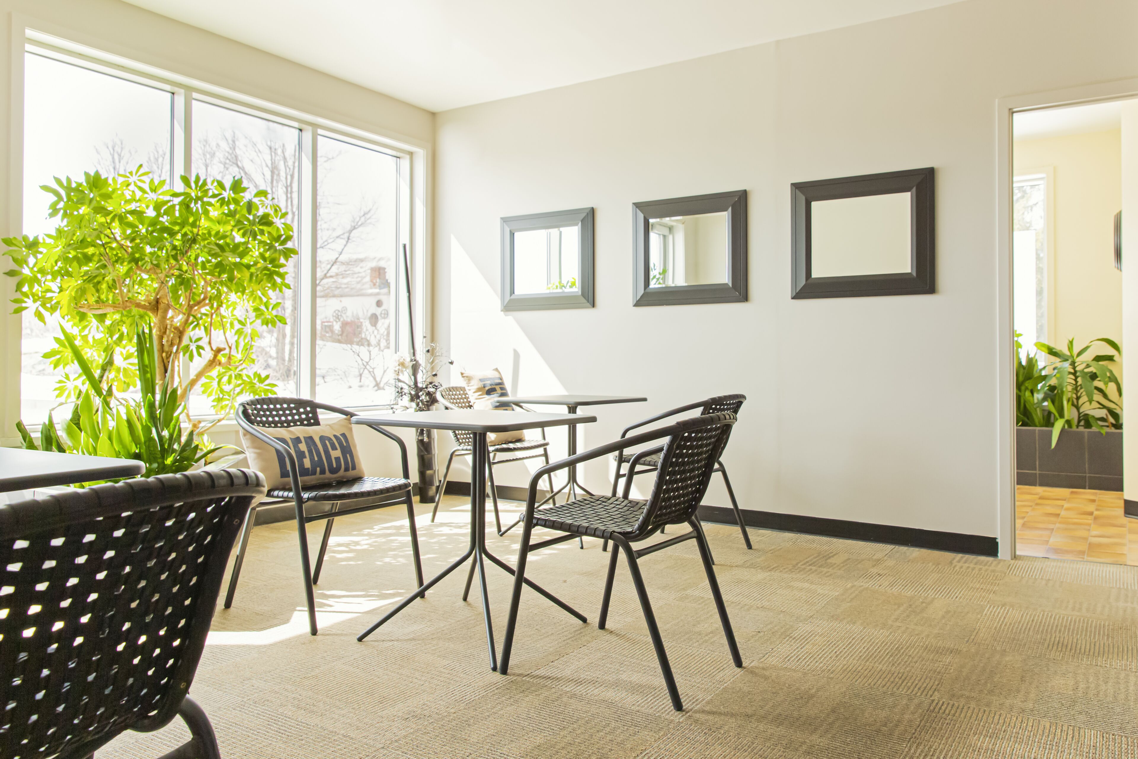 Una habitación moderna con un ventanal grande, una mesa de comedor, cuatro sillas y tres espejos enmarcados en la pared.