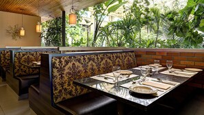 A restaurant with booths and a long table set for dining, featuring a view of lush greenery through large windows. - Hotel L'Oiseliere Montmagny (Montmagny)