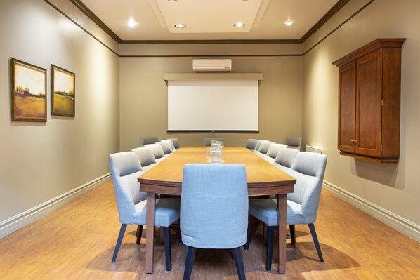 Un salón de conferencias con una mesa de madera, seis sillas, una pantalla de proyector y un armario.