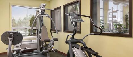 A gym with exercise equipment, large windows, and a view of trees and buildings outside.