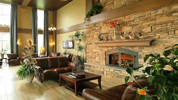 Un salón amplio con sofás de cuero, chimenea, paredes de piedra y ventanas grandes.