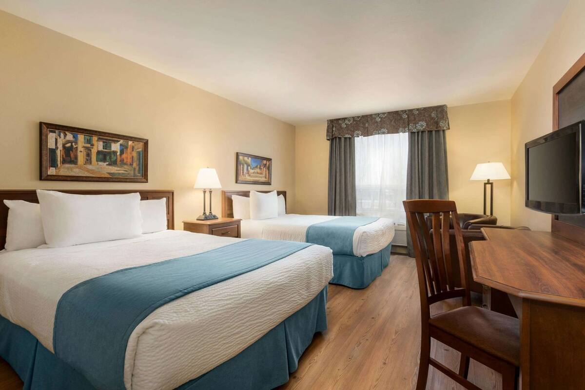 Habitación de hotel con dos camas, un escritorio, un televisor y dos cuadros en la pared.
