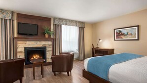 Una habitación de hotel con chimenea, una cama con manta azul, un televisor y un cuadro en la pared.