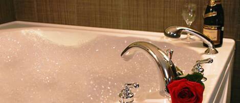 A bathtub with multiple faucets, a rose, and a bottle of champagne.