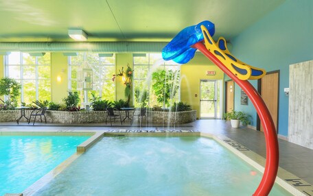 An indoor swimming pool with a water slide, surrounded by indoor seating and large windows.