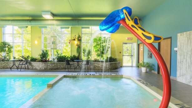 Una piscina interior con tobogán de agua, rodeada de asientos interiores y ventanas amplias.