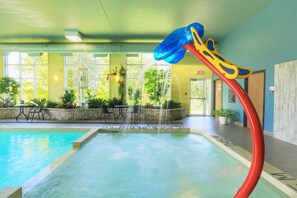 Une piscine intérieure avec un toboggan, entourée d’espaces de détente et de grandes fenêtres.
