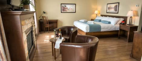 Habitación de hotel con cama, un sillón de cuero, una mesita con una botella y vasos, una silla y una chimenea.