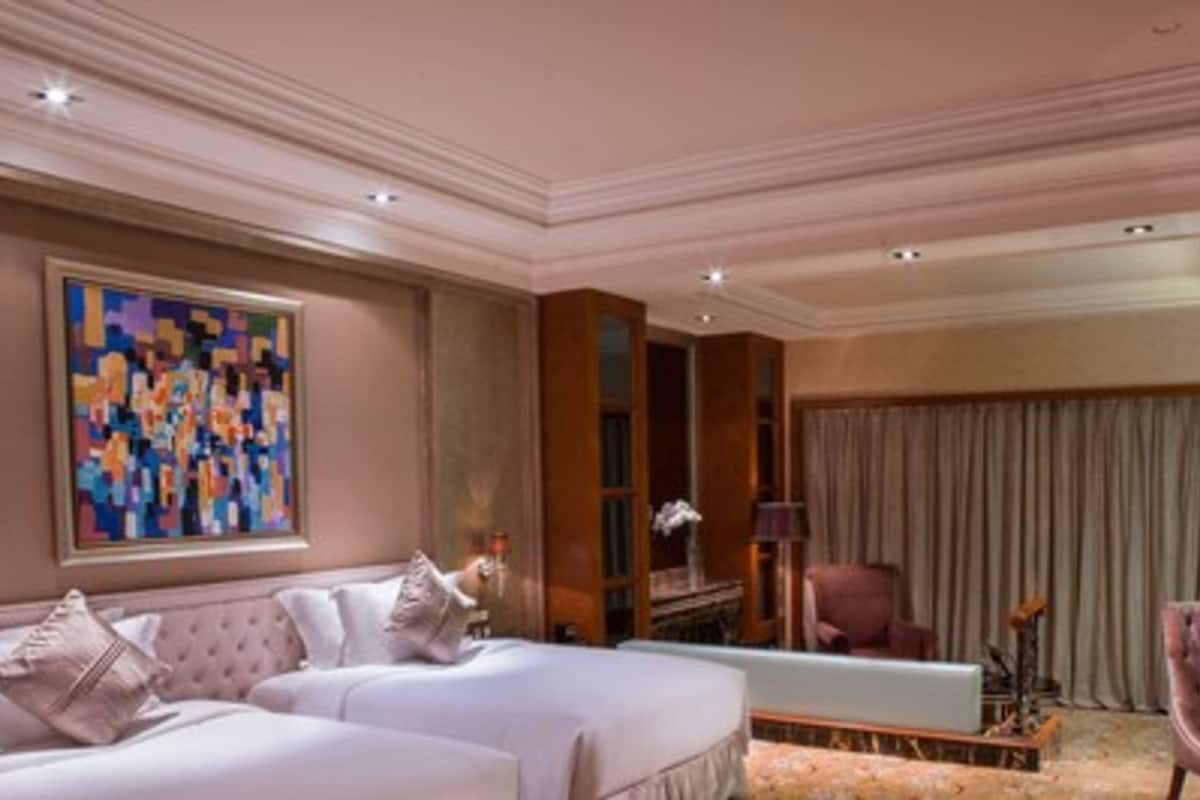 Ein Hotelzimmer mit zwei Betten, einem großen abstrakten Gemälde, einem Schreibtisch mit Lampe und einem Sessel.