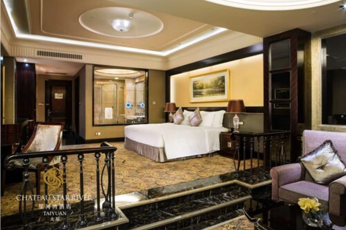 Ein Hotelzimmer mit einem großen Bett, einer Sitzecke inklusive Sofa, einem Couchtisch und einer dekorativen Geländer.