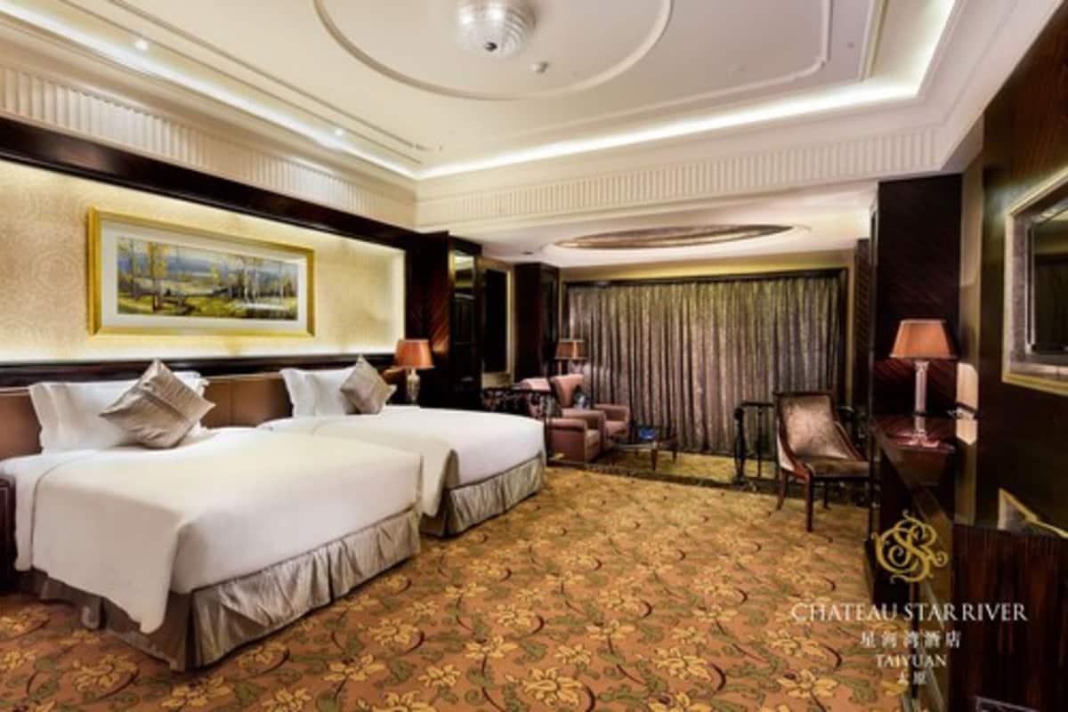 Ein Hotelzimmer mit zwei Betten, einem großen Gemälde an der Wand, einer Chandelüster und Blick auf die Stadt.