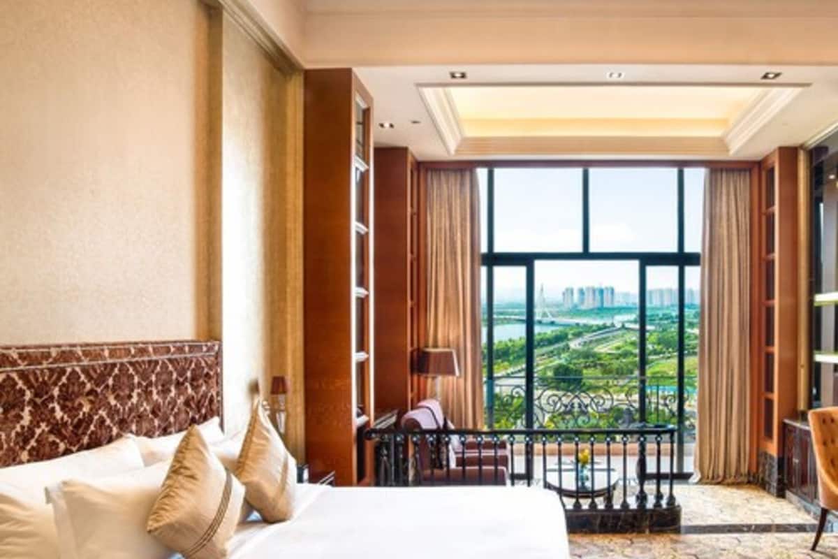 Ein Hotelzimmer mit einem großen Bett, Blick auf eine Stadtlandschaft und einem Balkon mit Geländer.