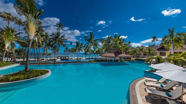A resort pool with palm trees, lounge chairs, and a view of the ocean. - Henann Resort Alona Beach (Panglao)