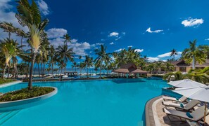 Piscina de resort con palmeras, sillas de descanso y vista al océano.