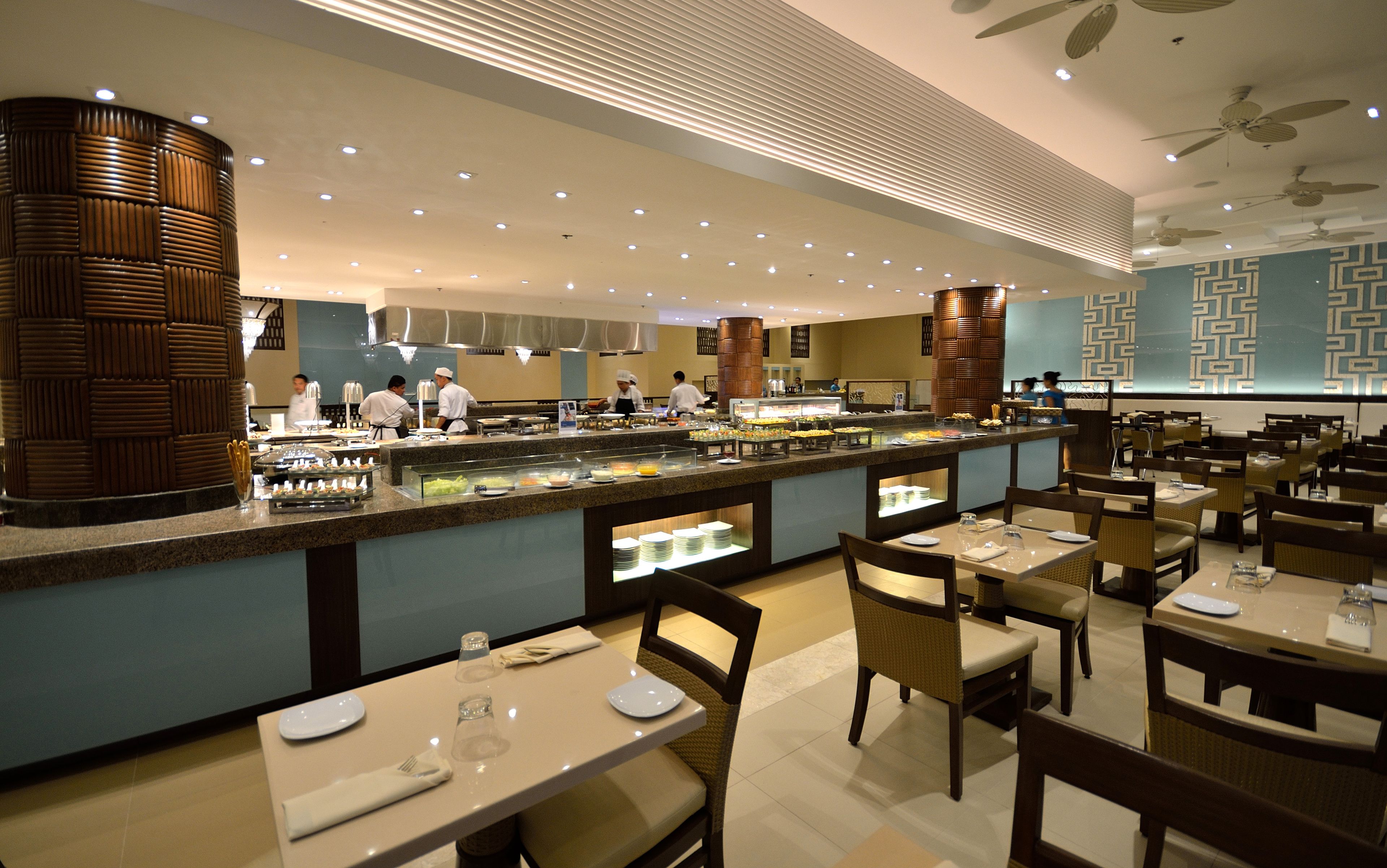 Een buffetgedeelte met diverse food stations, een balie met bediening en eettafels met stoelen.