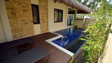 A pool area with a wooden deck, a thatched roof structure, and a view of palm trees.