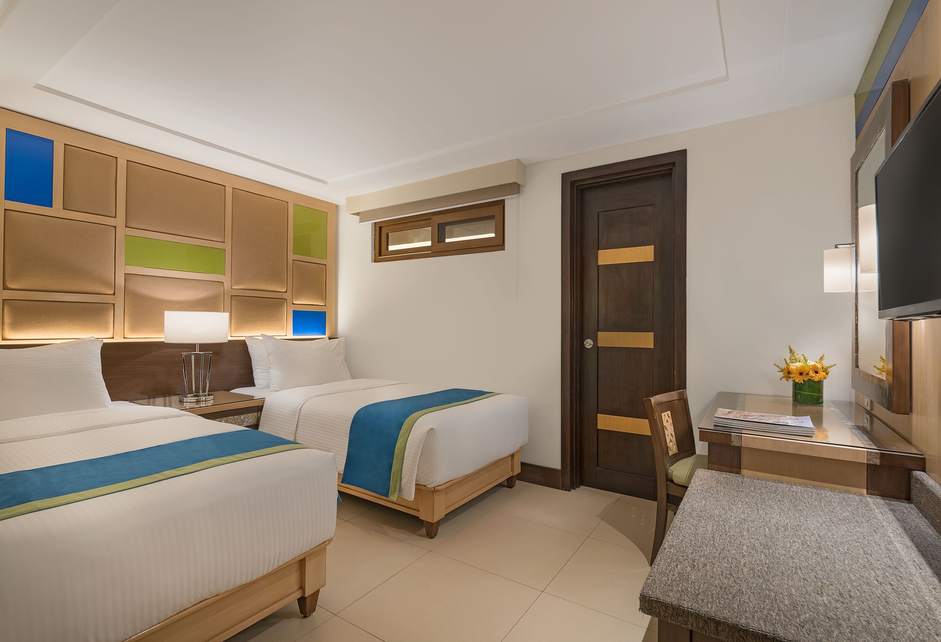 Habitación de hotel con dos camas, un escritorio, una silla, un televisor y una puerta.
