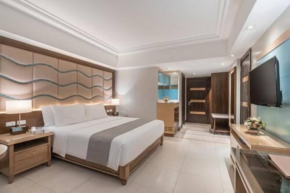 A modern hotel room with a large bed, a nightstand, a TV, and a wardrobe.