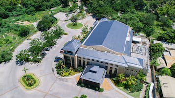 An aerial view of a building with a flat roof, surrounded by greenery and a parking lot.