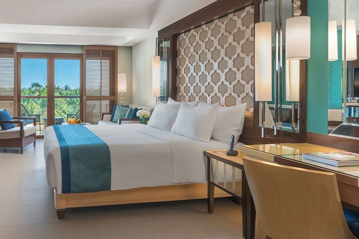 A hotel room with a large bed, a desk, a TV, and a balcony with a view of the outdoors.
