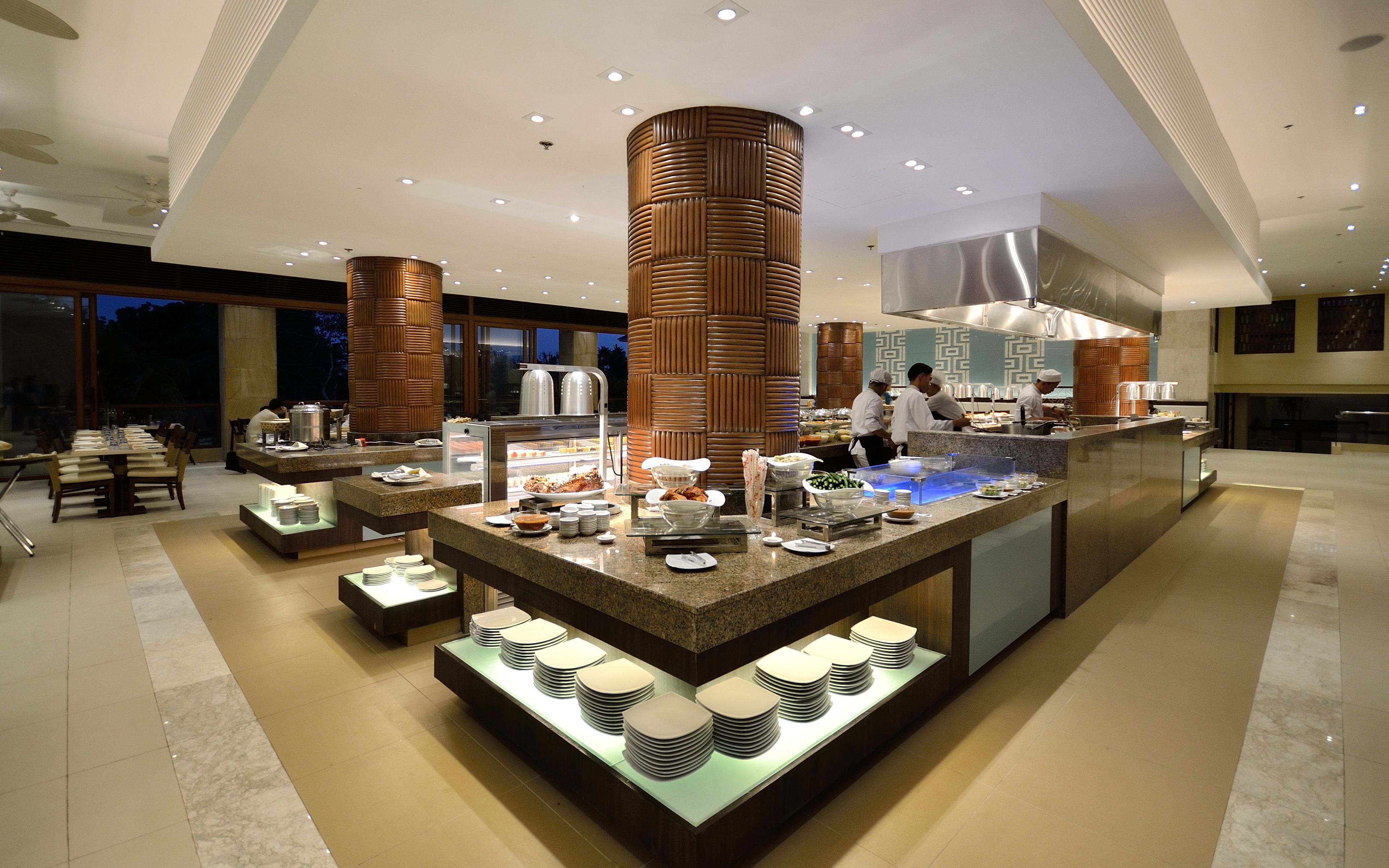 A modern buffet setup with a central island, multiple serving stations, and a seating area with tables and chairs.