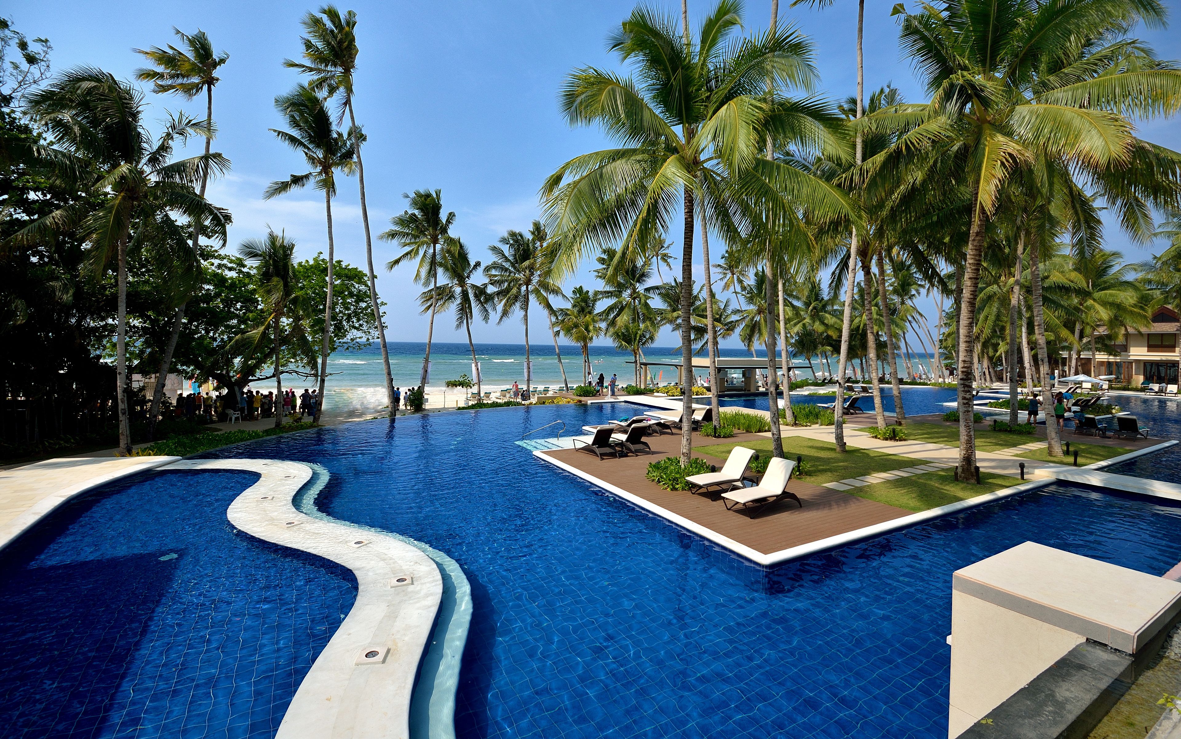 A resort pool area with a winding pool design, lounge chairs, and palm trees.