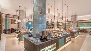 A modern hotel lobby with a central buffet area, decorative lighting, and a large cylindrical column. - Henann Resort Alona Beach (Panglao)