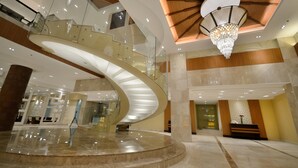 A modern hotel lobby with a curved staircase, a chandelier, and a reception desk. - Henann Resort Alona Beach (Panglao)