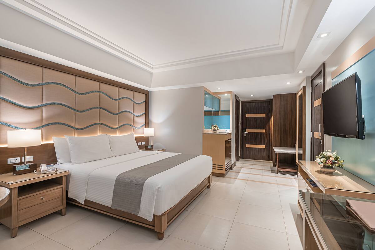 A modern hotel room with a large bed, bedside tables, a TV, and a bathroom visible through an open door.