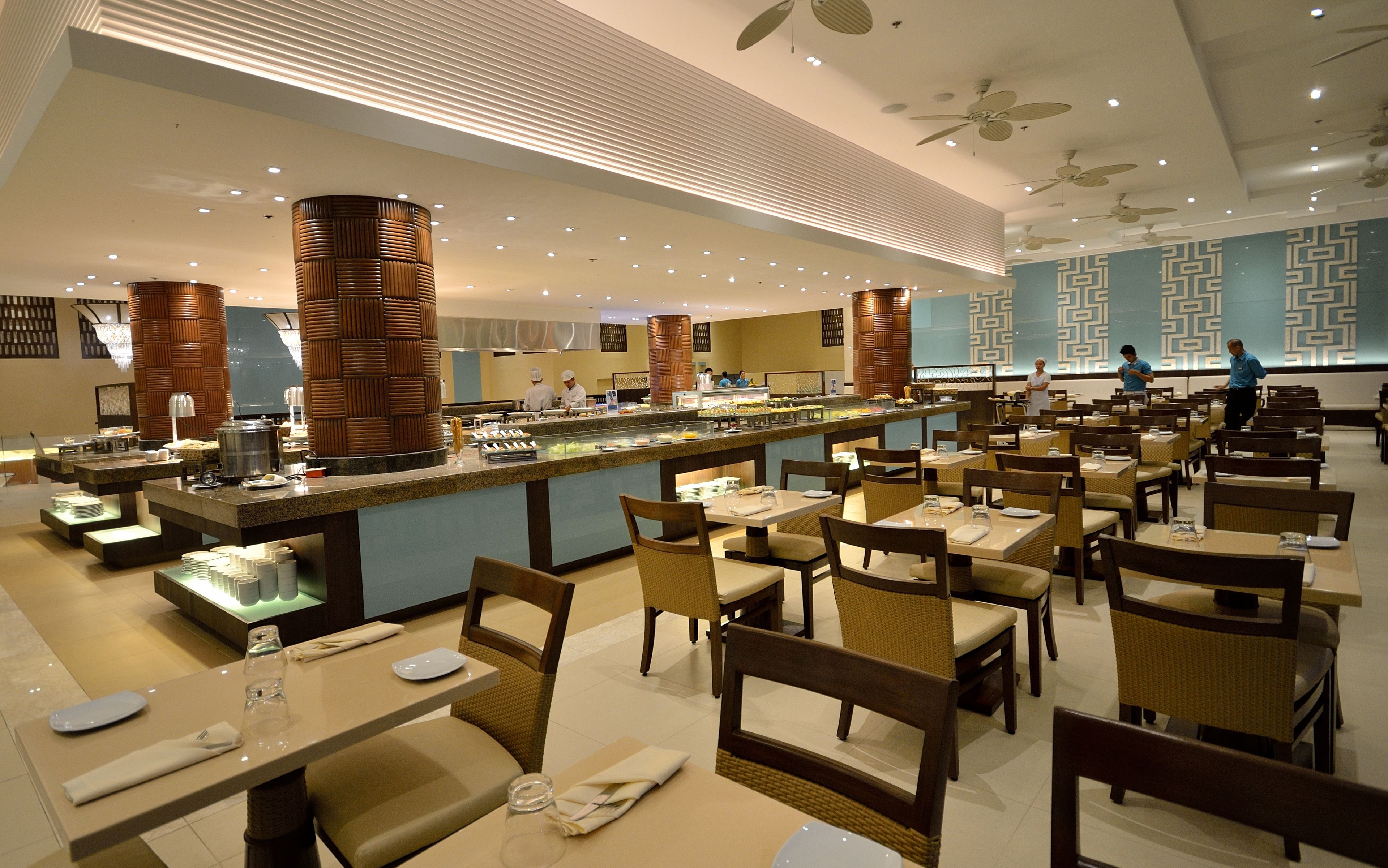 A modern restaurant with a buffet, multiple dining tables, and ceiling fans.