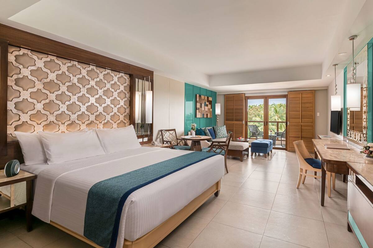 A hotel room with a large bed, a desk, a chair, and a television.