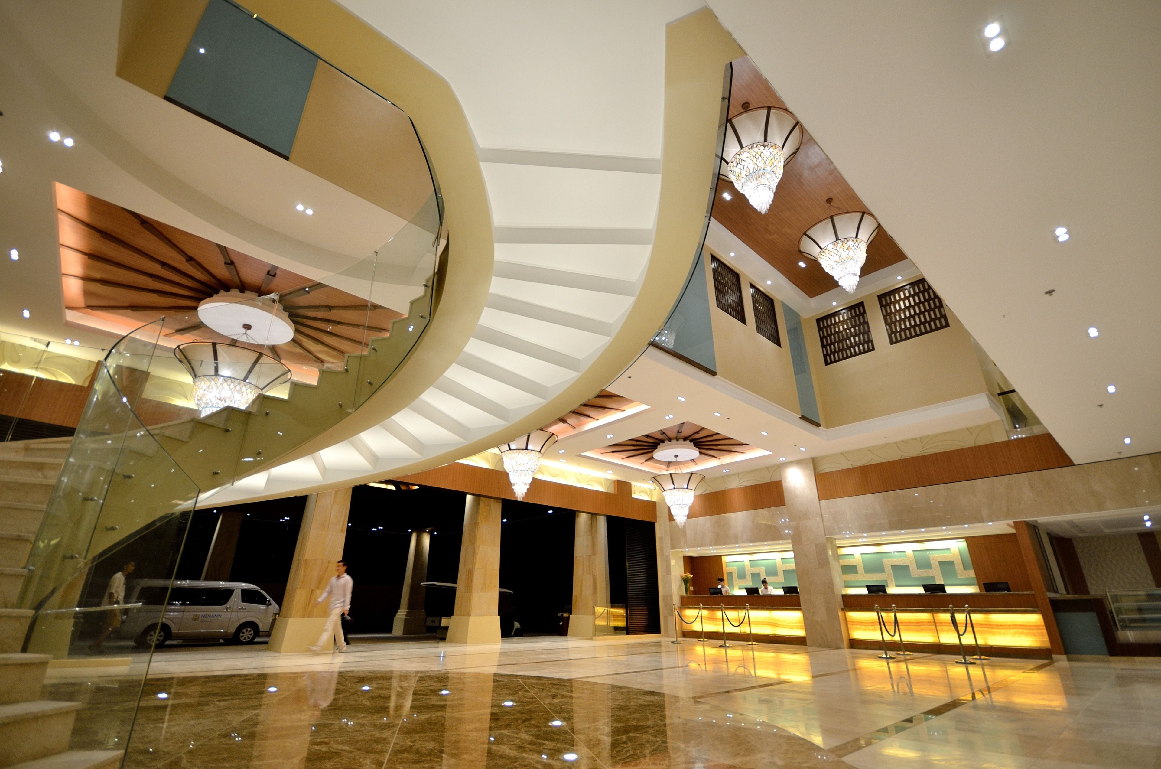 A spacious lobby with a grand staircase, a reception desk, and a modern chandelier.
