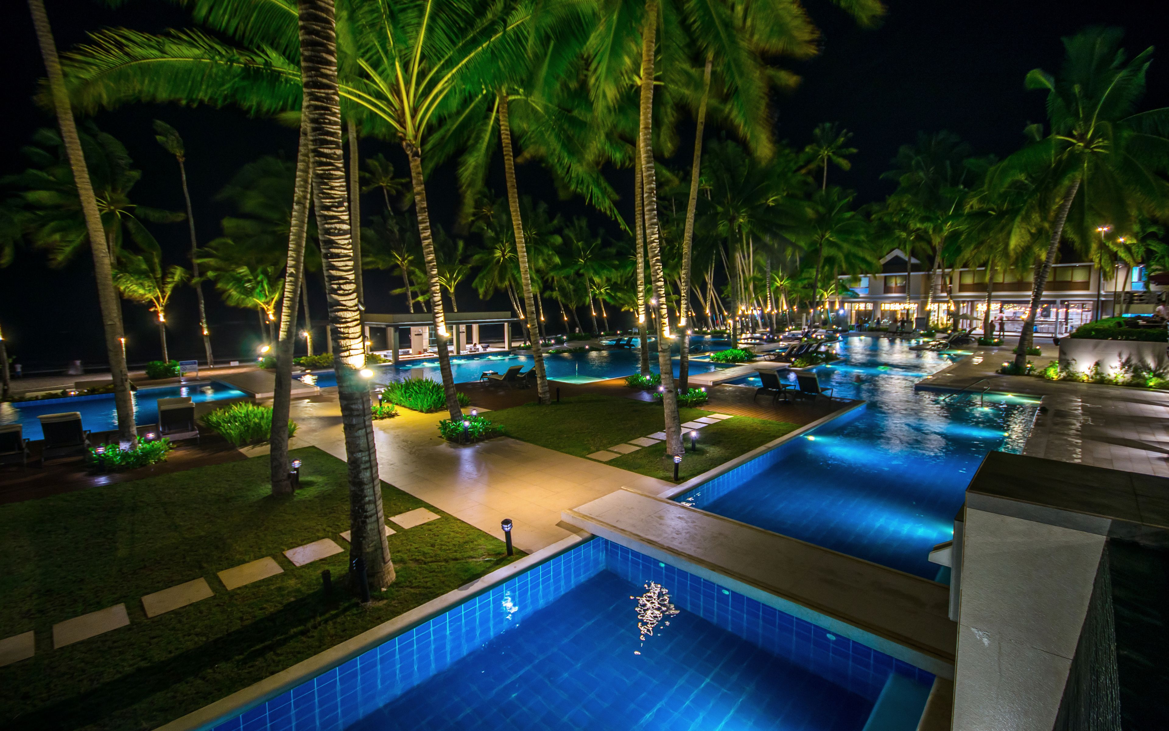 A nighttime resort with multiple swimming pools, palm trees, and well-lit pathways.