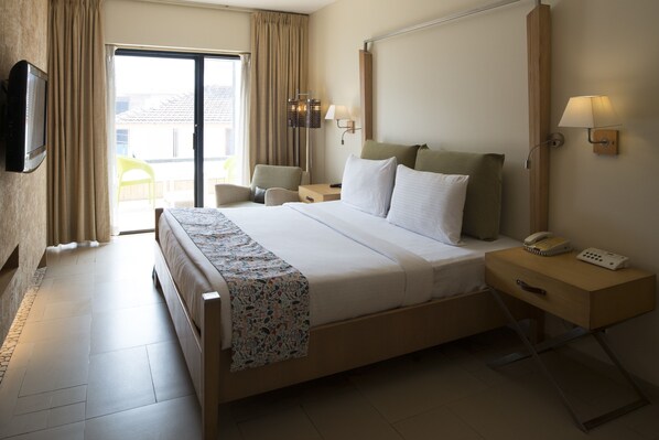 A hotel room with a large bed, bedside tables, a TV, and a view of the outside.