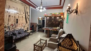 A living room with a sofa, chairs, a coffee table, a TV, and a wall mural. - Meramees Hostel (Cairo)