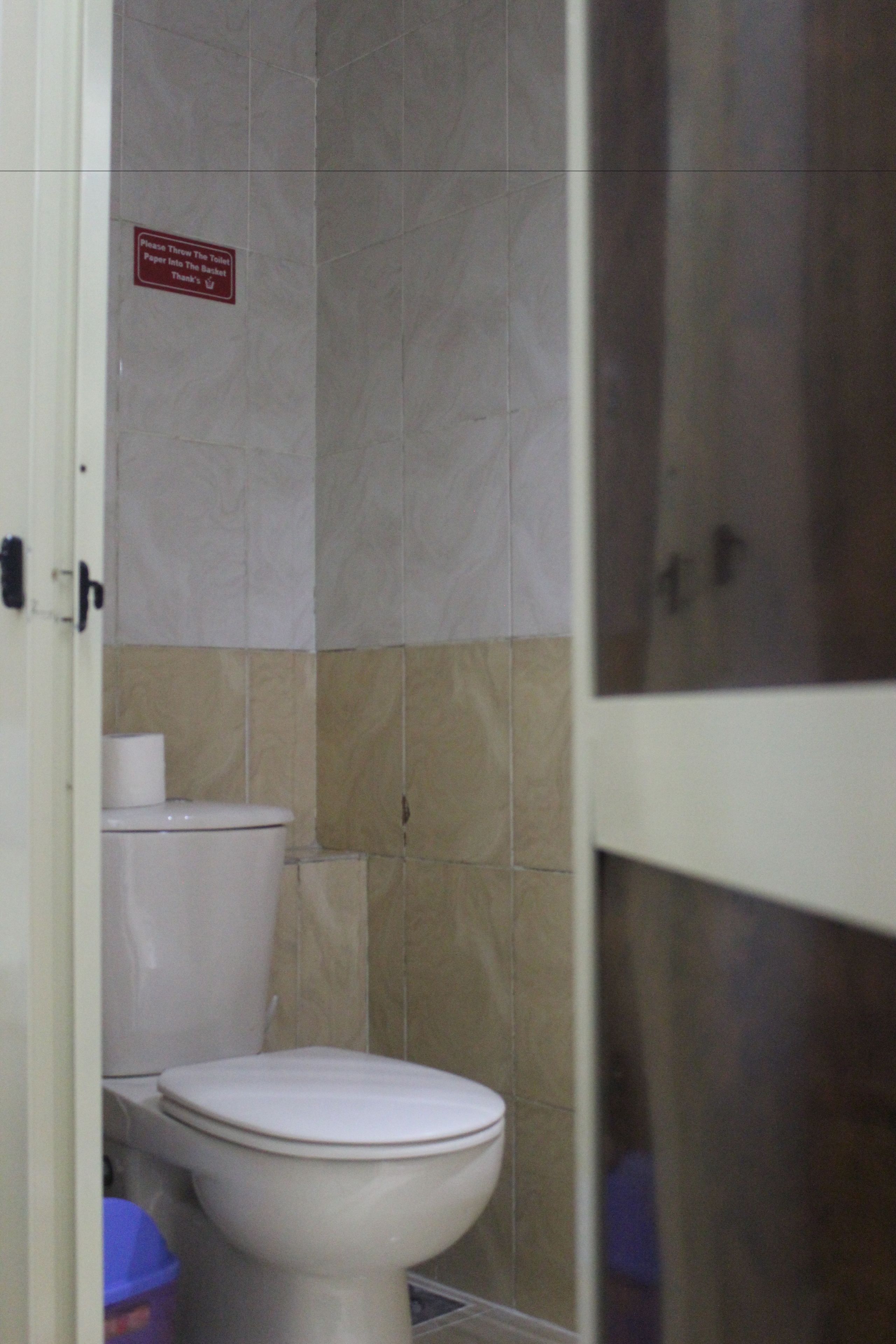 A bathroom with a toilet, a roll of toilet paper, and a trash bin.