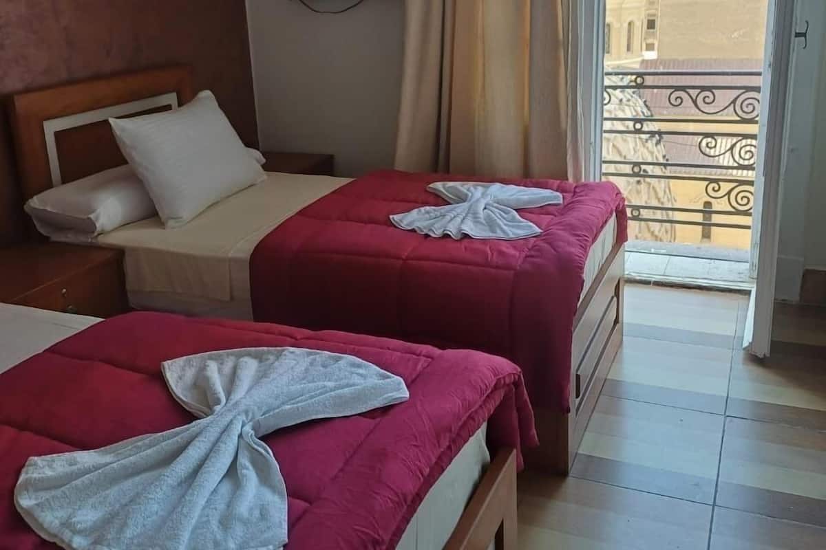 Habitación de hotel con dos camas, un televisor en la pared y un balcón con vistas a edificios.