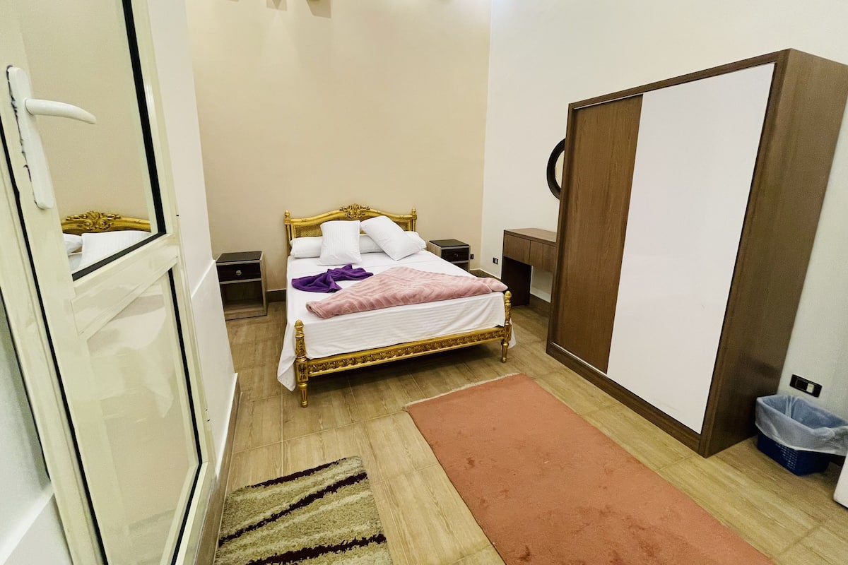 Un dormitorio con cama, mesitas de noche, un armario y un escritorio pequeño.