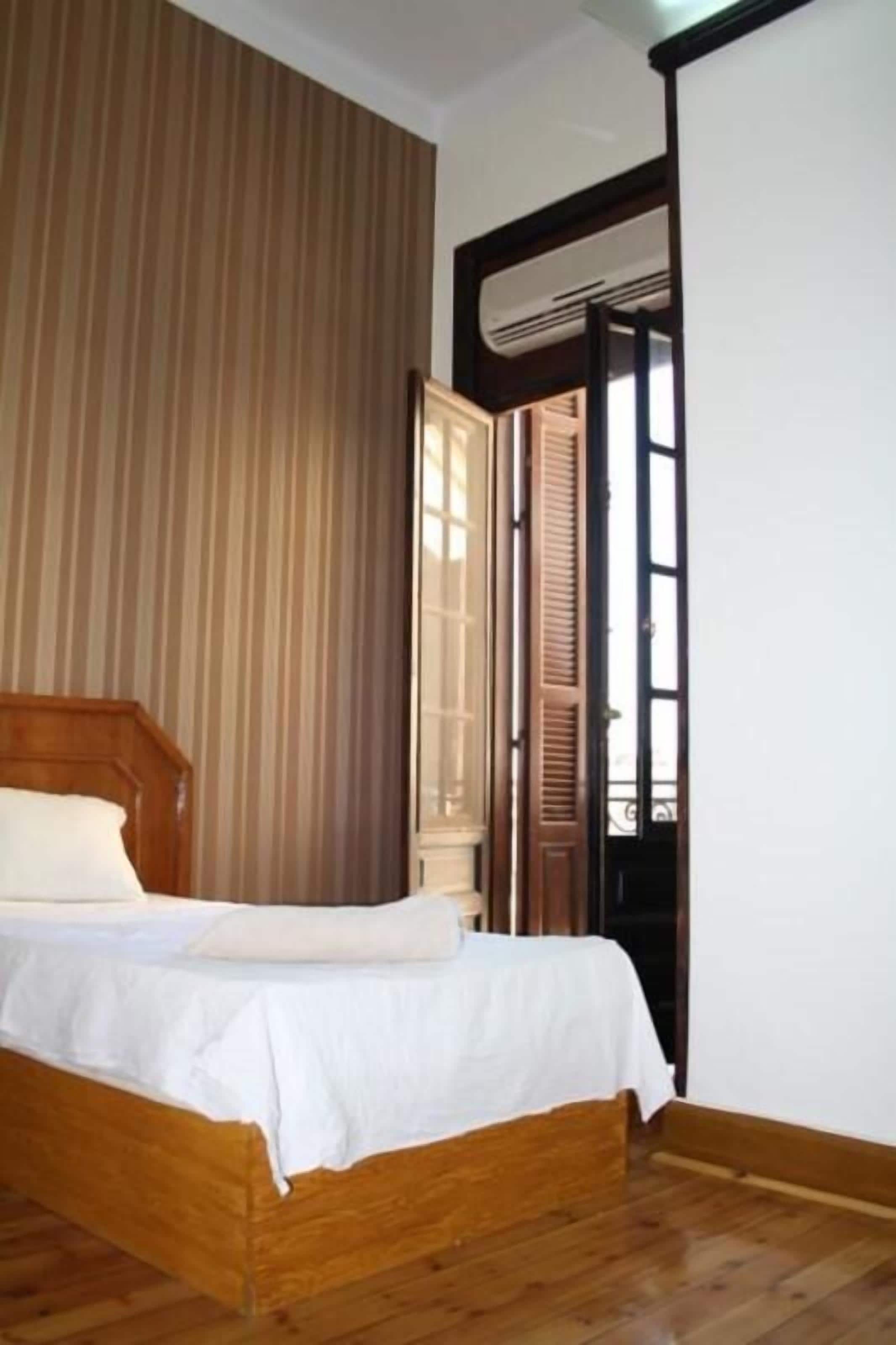 Ein Schlafzimmer mit einem hölzernen Bett, einem Fenster mit Jalousien und einer Tür zu einem anderen Raum.