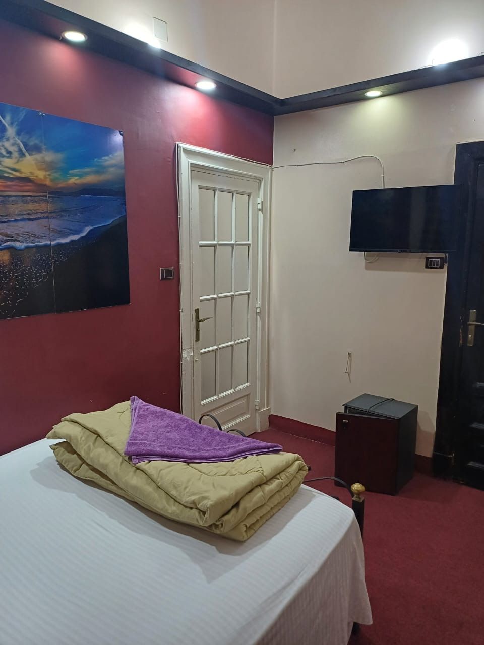 A bedroom with a bed, a door, a TV, and a small table.