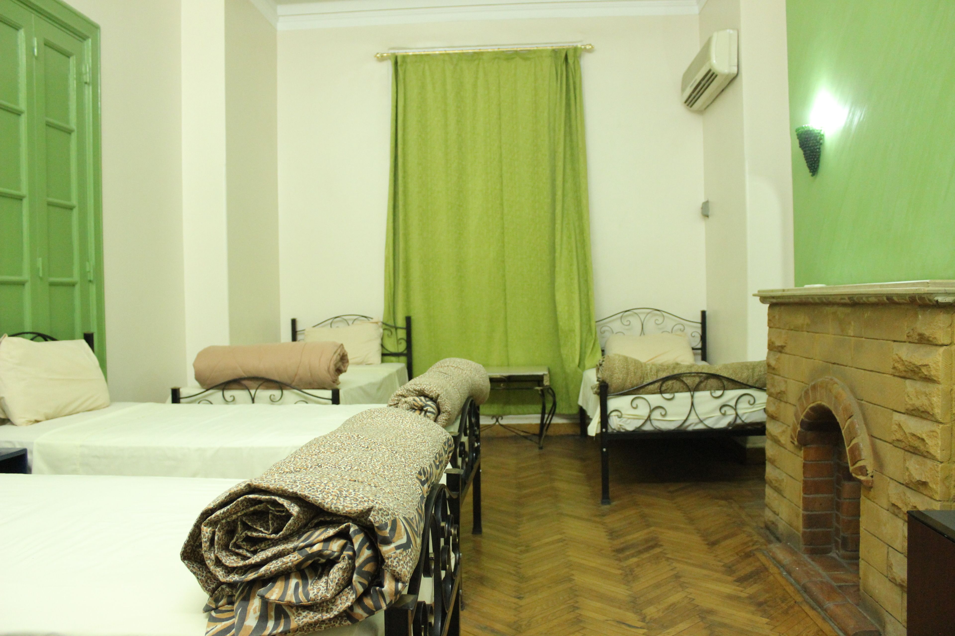 Une chambre avec deux lits, un rideau vert, une cheminée en briques et un appareil de climatisation blanc.