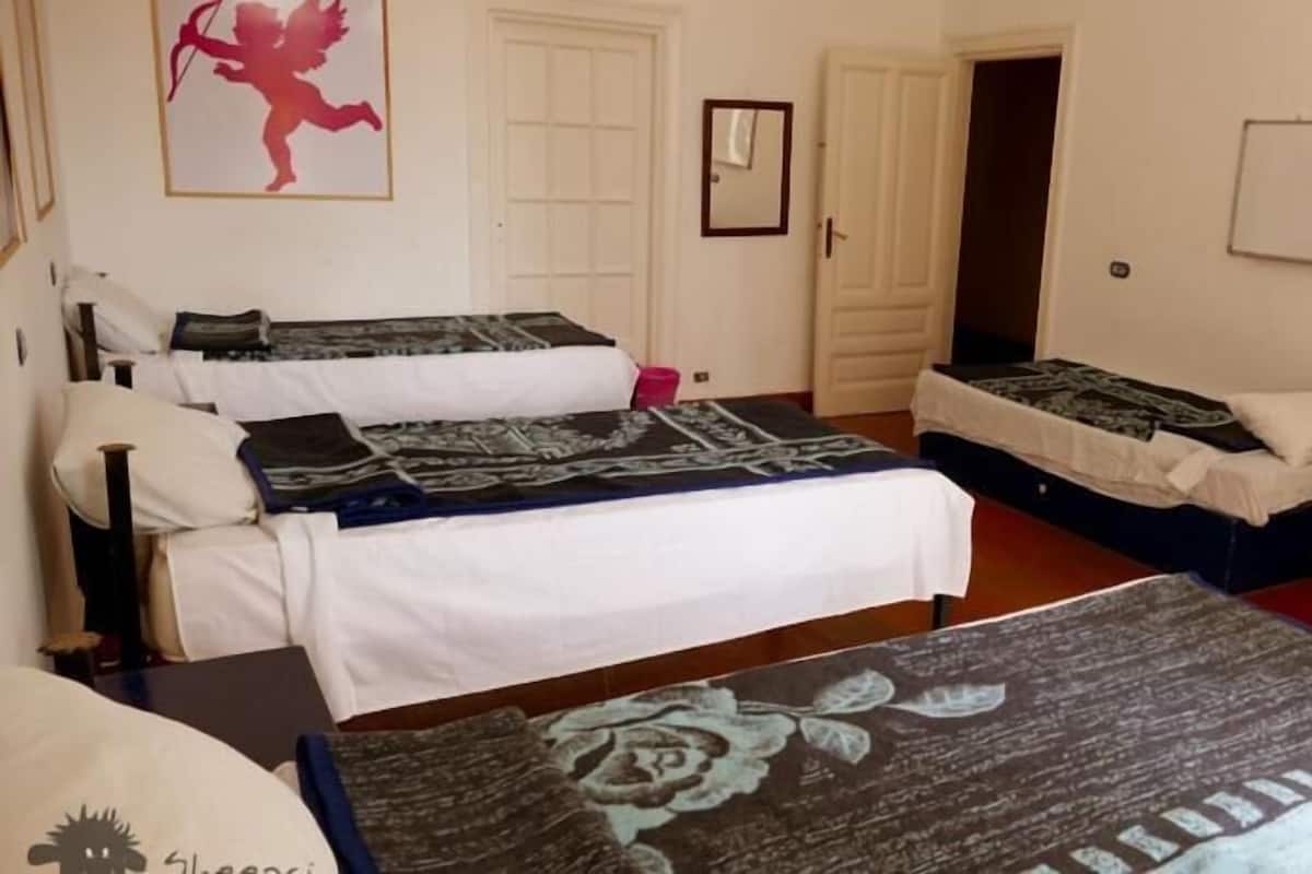 Una habitación con tres camas, cada una con diferente colcha estampada. Hay un cuadro en la pared y una puerta que da a otra habitación.